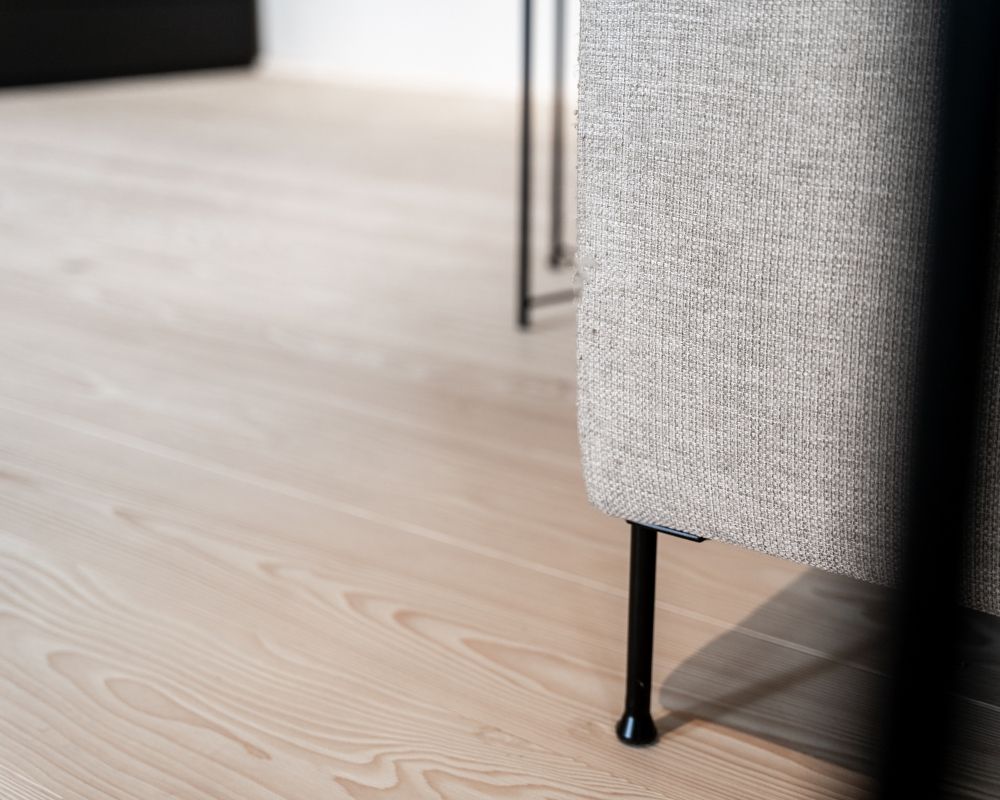 Nahaufnahme eines Weisstanne Holzbodens neben einem grauen Sofa mit schlanken schwarzen Metallbeinen.