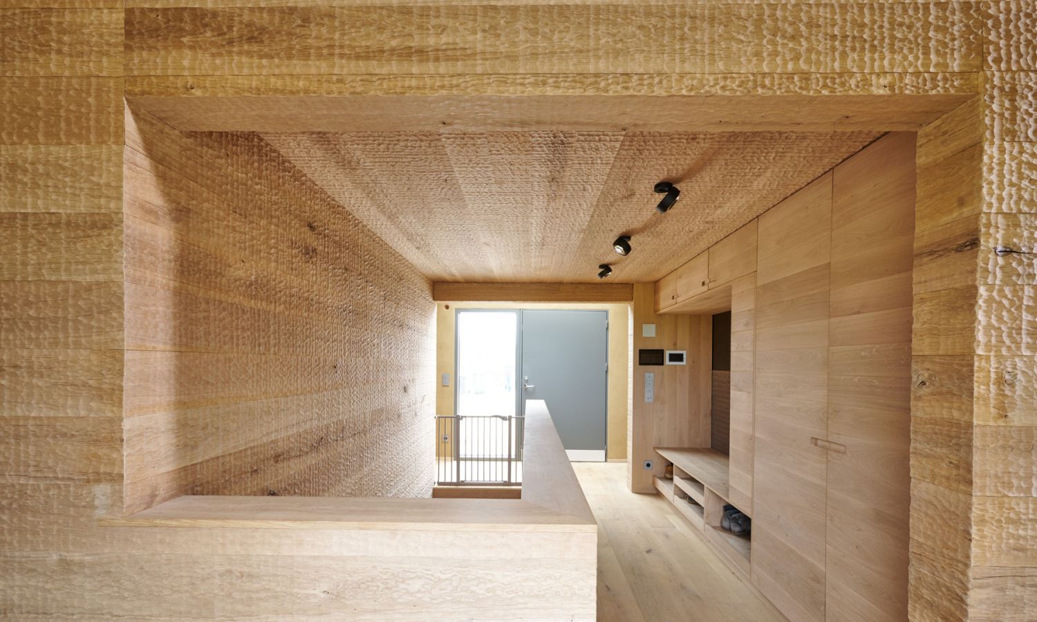 Innenraum mit hellen Holzverkleidungen an Waenden; Decke und Boden; rechteckiger Durchgang mit Gelaender und Fenster im Hintergrund