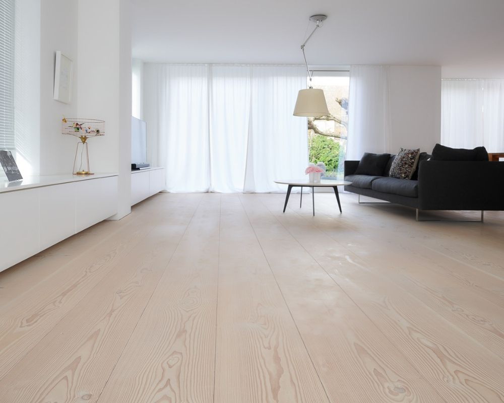 Espace de vie lumineux et ouvert avec une grande fenêtre; canapé noir; table ronde et lampe suspendue; sol en douglas