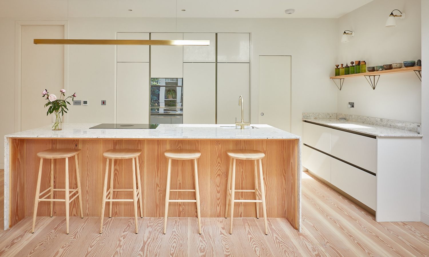 Modern kitchen with Douglas fir wooden floor, kitchen island with four wooden stools, white fronts, and long, narrow ceiling light.