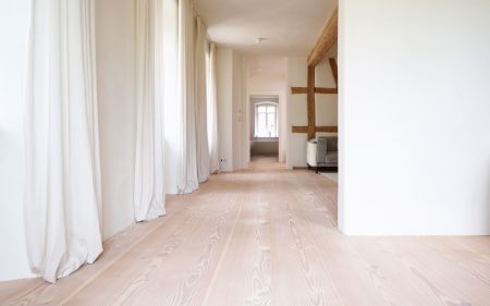 Heller Flur mit Douglasie Holzboden; weißen Wänden; langen weißen Vorhängen an den Fenstern; sichtbaren Holzbalken an der Decke