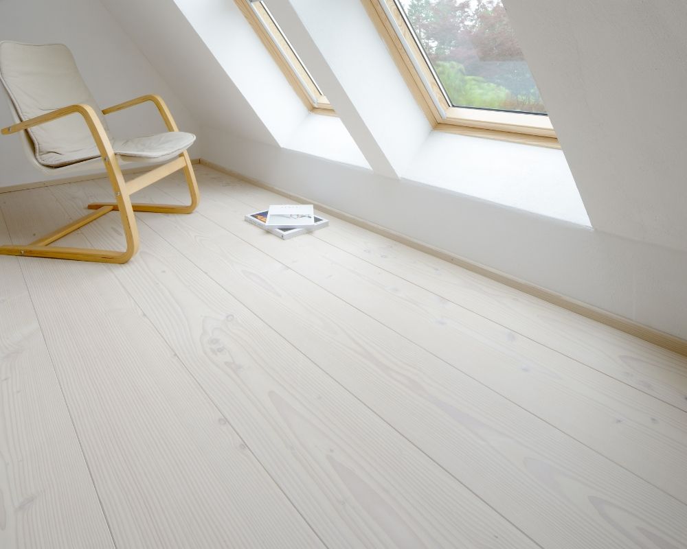 Pièce lumineuse avec fenêtre de toit inclinée; sol en bois blanc; chaise avec structure en bois; coussin d’assise blanc