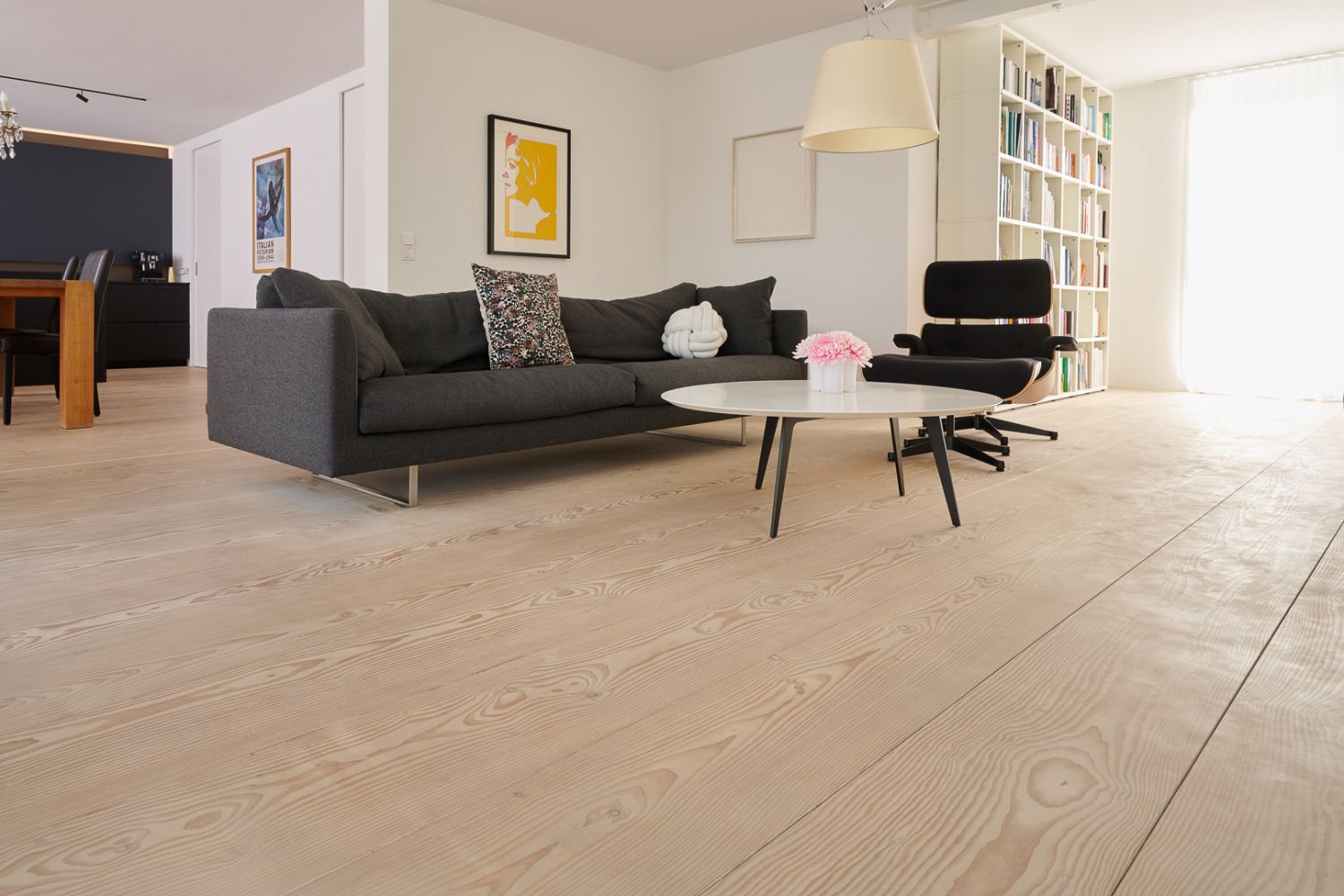 Wohnzimmer mit grauem Sofa; rundem weißen Couchtisch; schwarzem Sessel und hellem Holzboden