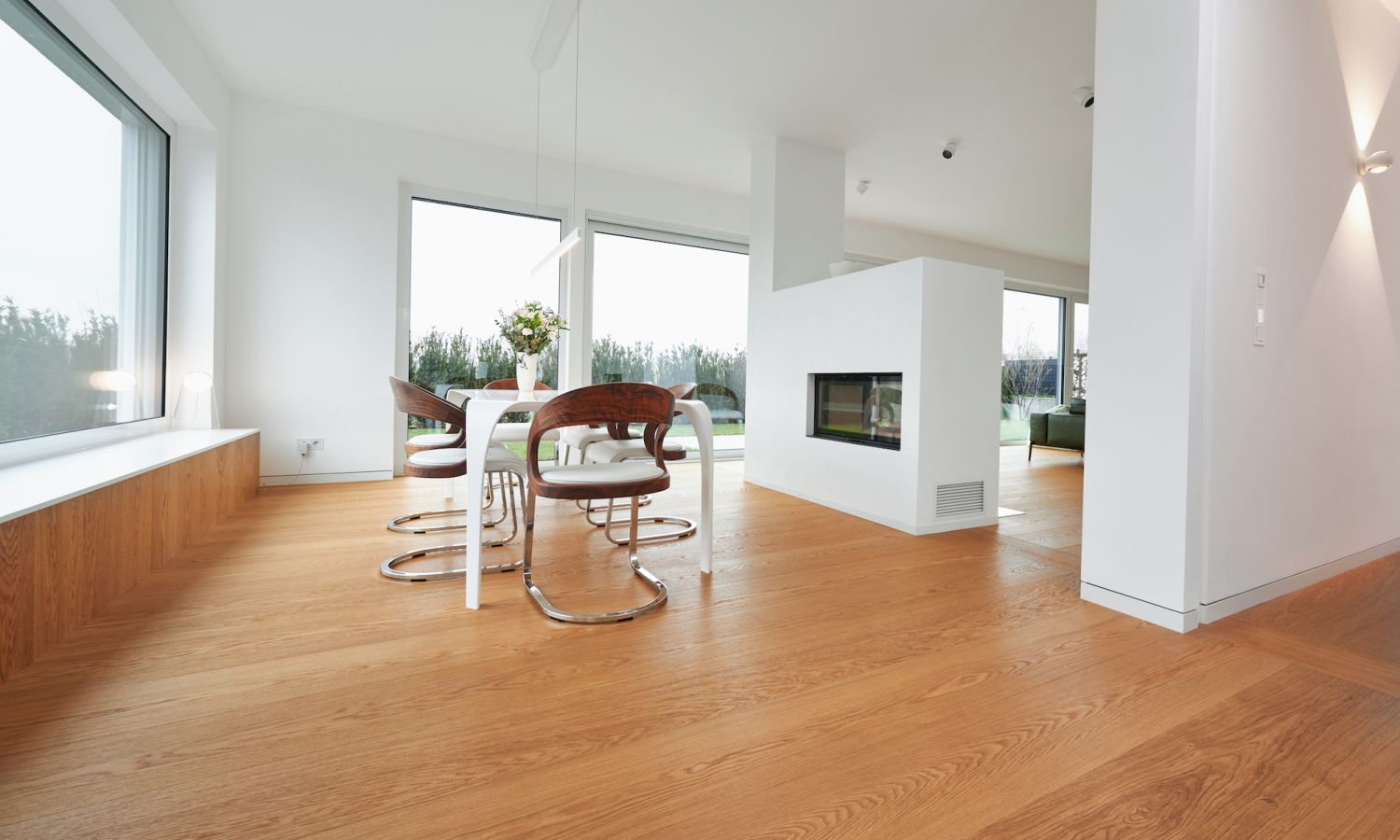 Modern dining area with white table, brown chairs with metal frames, and centrally built fireplace in a bright room with large windows