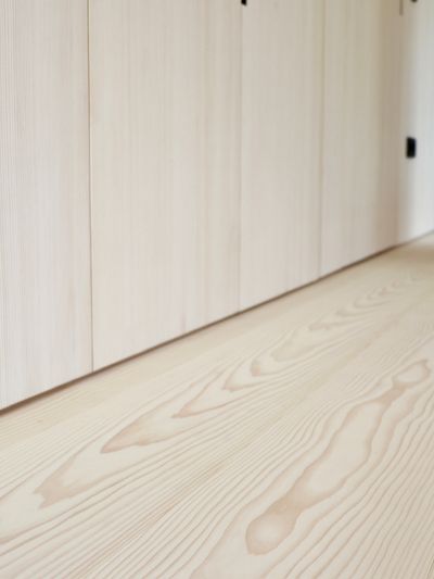View of a white fir wooden floor with visible grain and a wall with light-colored cabinet doors in a corridor.