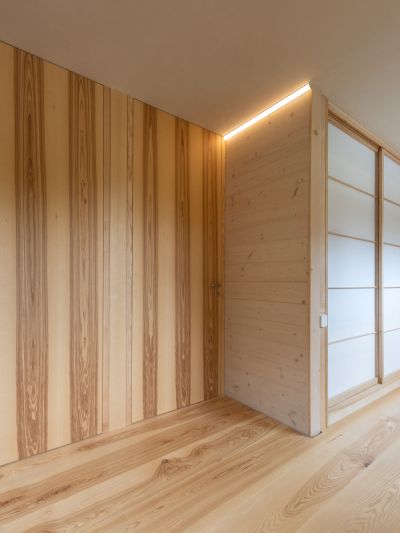 Modern interior with light wood panels on walls and ash wood floor, integrated door and illuminated ceiling section.