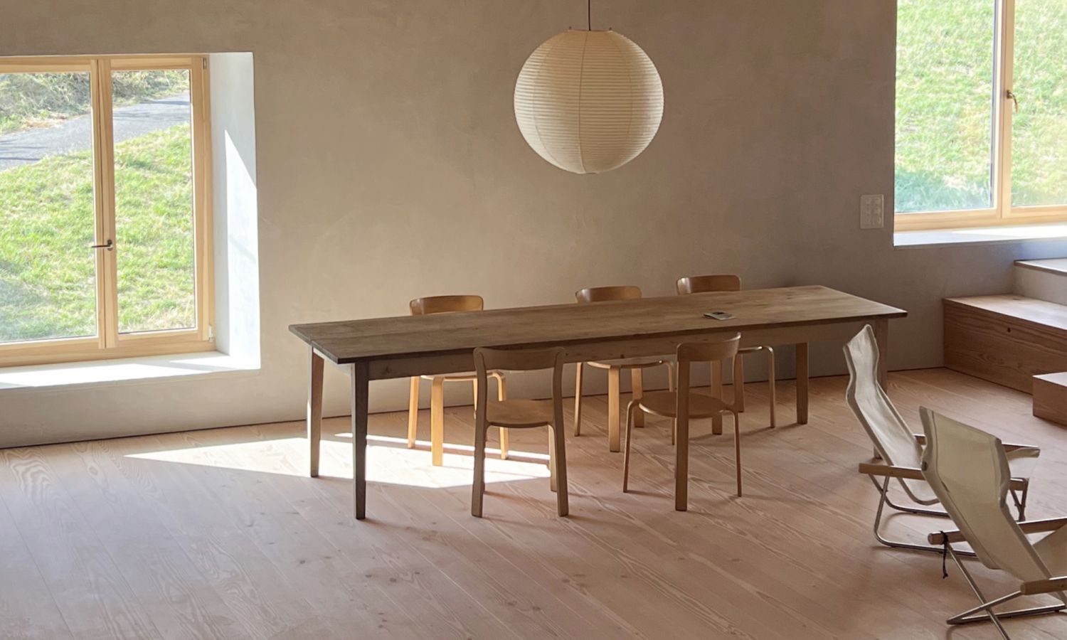 Une salle à manger dans une ferme rénovée avec de larges lames en sapin Douglas. Elle est équipée d’une table en bois simple, de chaises en bois modernes et d’une grande lampe ronde blanche.