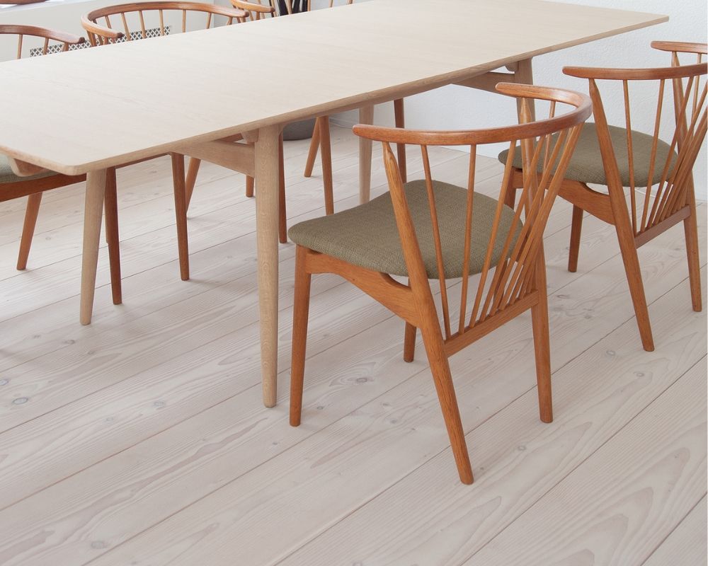 Table en bois avec pieds fins; chaises en bois avec coussins d’assise verts; sol en bois clair de douglas