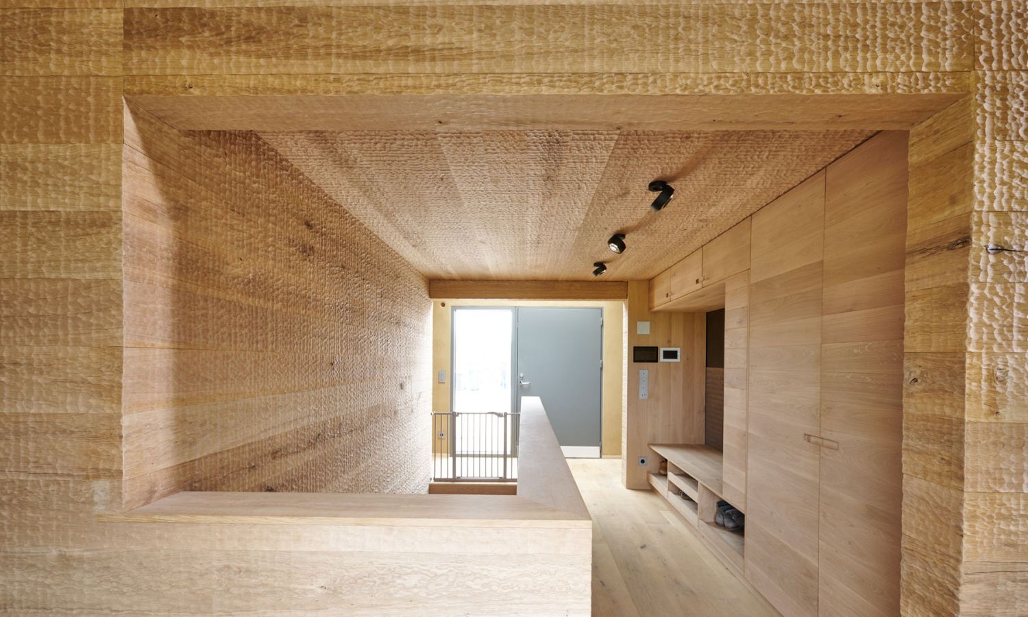 Innenraum mit hellen Holzverkleidungen an Waenden; Decke und Boden; rechteckiger Durchgang mit Gelaender und Fenster im Hintergrund