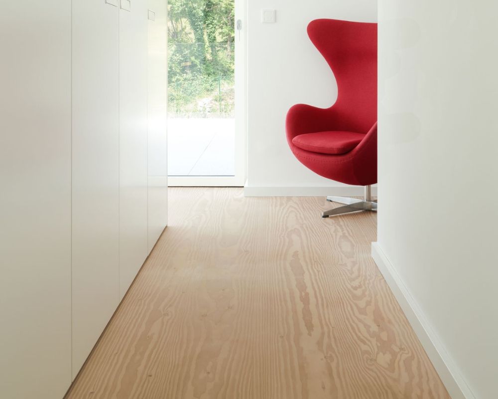 Fauteuil Egg rouge avec base en aluminium; dans un couloir lumineux avec sol en bois de douglas; murs blancs