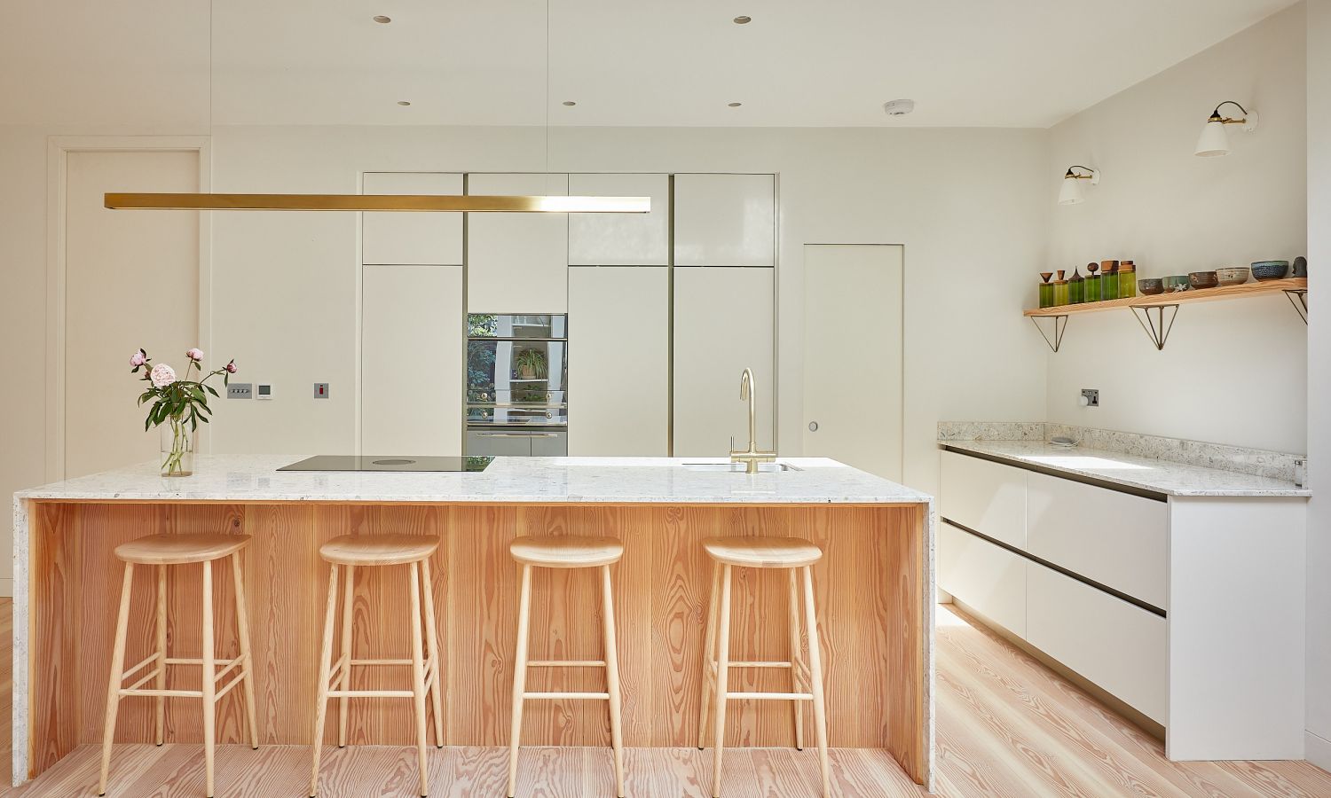 Cuisine moderne avec sol en bois de douglas, îlot avec quatre tabourets en bois, façades blanches et longue lampe de plafond étroite.