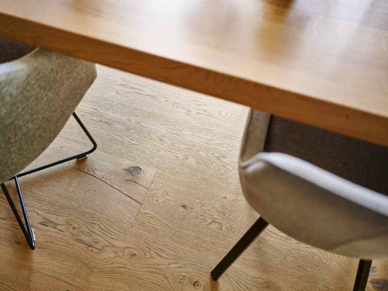 Two grey chairs with metal legs are at a wooden table on oak floorboards with visible grain.