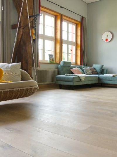 Großer Raum mit Blick Richtung Fenstern. In der hinteren Ecke steht ein türkises Sofa. Rechts hängt ein Hängesofa von der Decke.