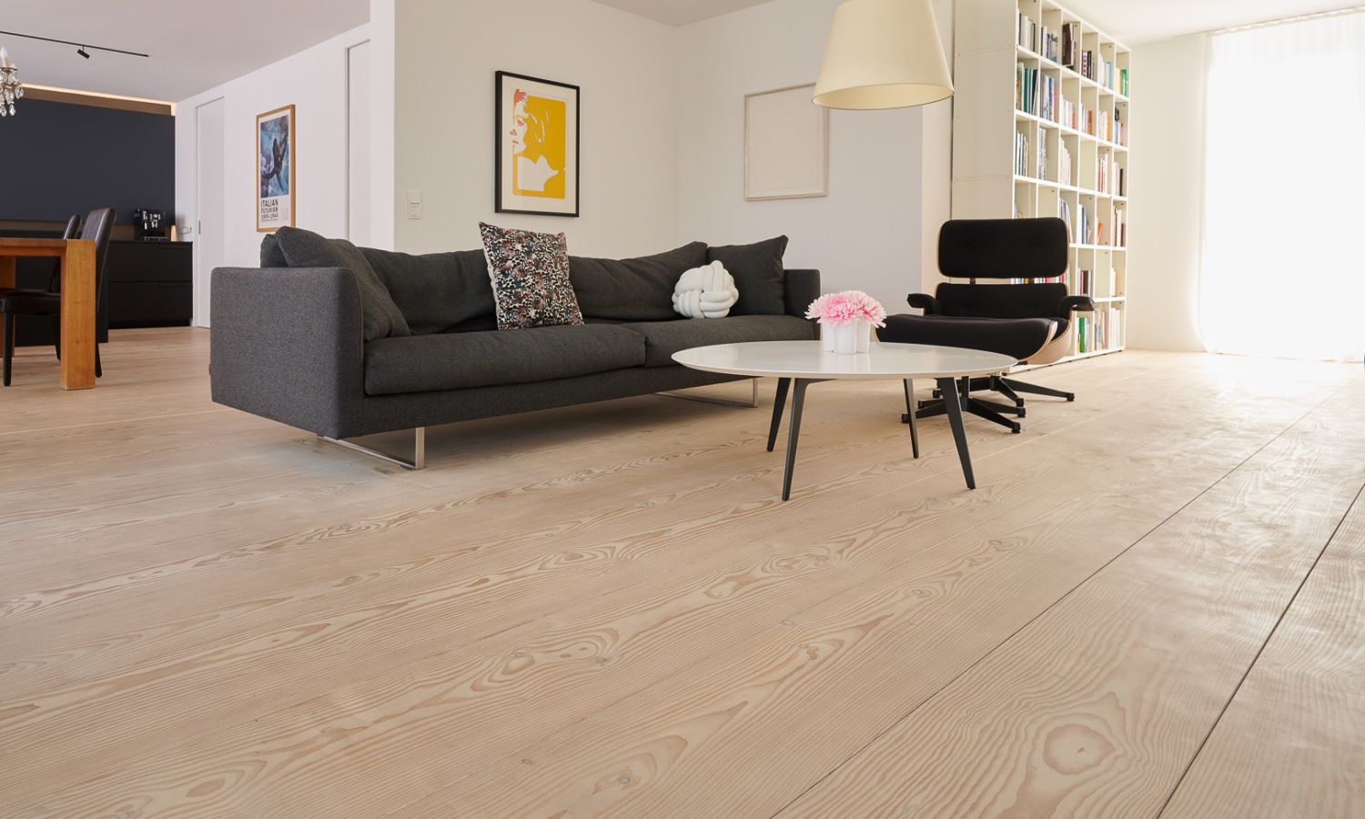 Salon avec canapé gris; table basse ronde blanche; fauteuil noir et sol en bois clair