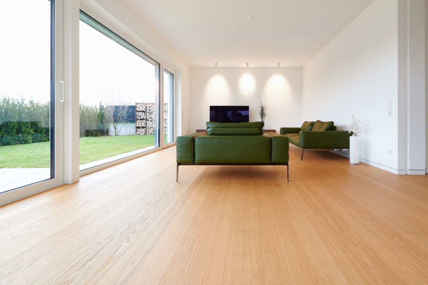 Moderner Wohnraum mit zwei gruenen Sofas, großem Fenster mit Blick auf Garten und Eiche Holzboden.