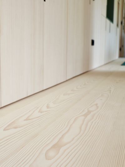 View of a white fir wooden floor with visible grain and a wall with light-colored cabinet doors in a corridor.