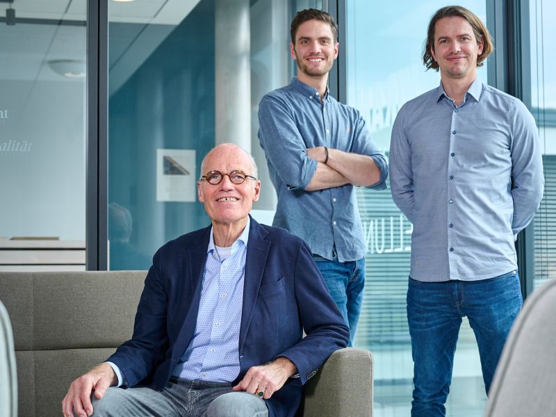 Familie von Saucken im Buro in einem modernen Buero, einer sitzt auf einem Sessel, zwei stehen dahinter vor grossen Fenstern.