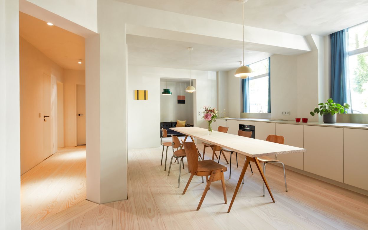 Esszimmer mit langem weißen Tisch; Holzstühlen; Blumenstrauß am Tisch; großen Fenstern mit blauen Vorhängen