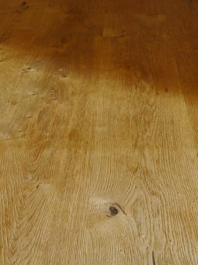 Nahaufnahme eines Holzbodens aus Eiche. Die Dielen sind in Sichtrichtung verlegt. Von rechts fällt ein Schatten auf den Boden.