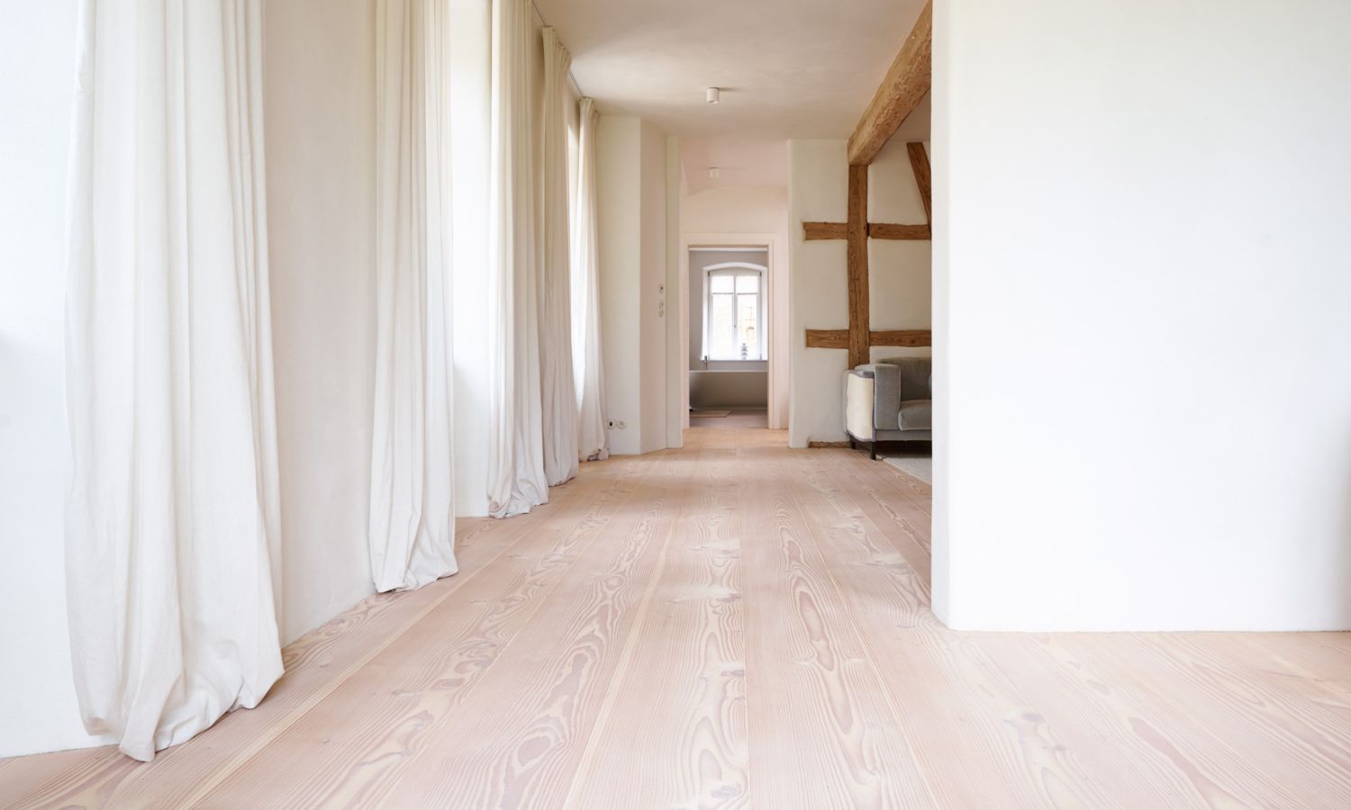 bright hallway with Douglas fir flooring; white walls; long white curtains on the windows; exposed wooden beams on the ceiling