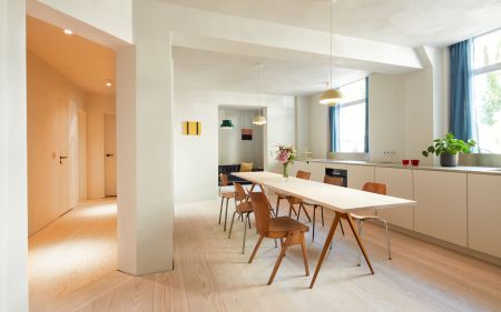 Esszimmer mit langem weißen Tisch; Holzstühlen; Blumenstrauß am Tisch; großen Fenstern mit blauen Vorhängen