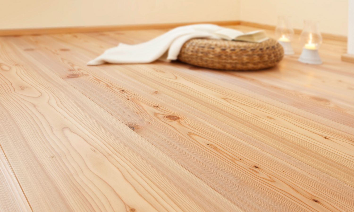 Nahaufnahme eines Lärche Holzbodens mit einem geflochtenen Korb, einer weißen Decke und einer Kerze im Hintergrund