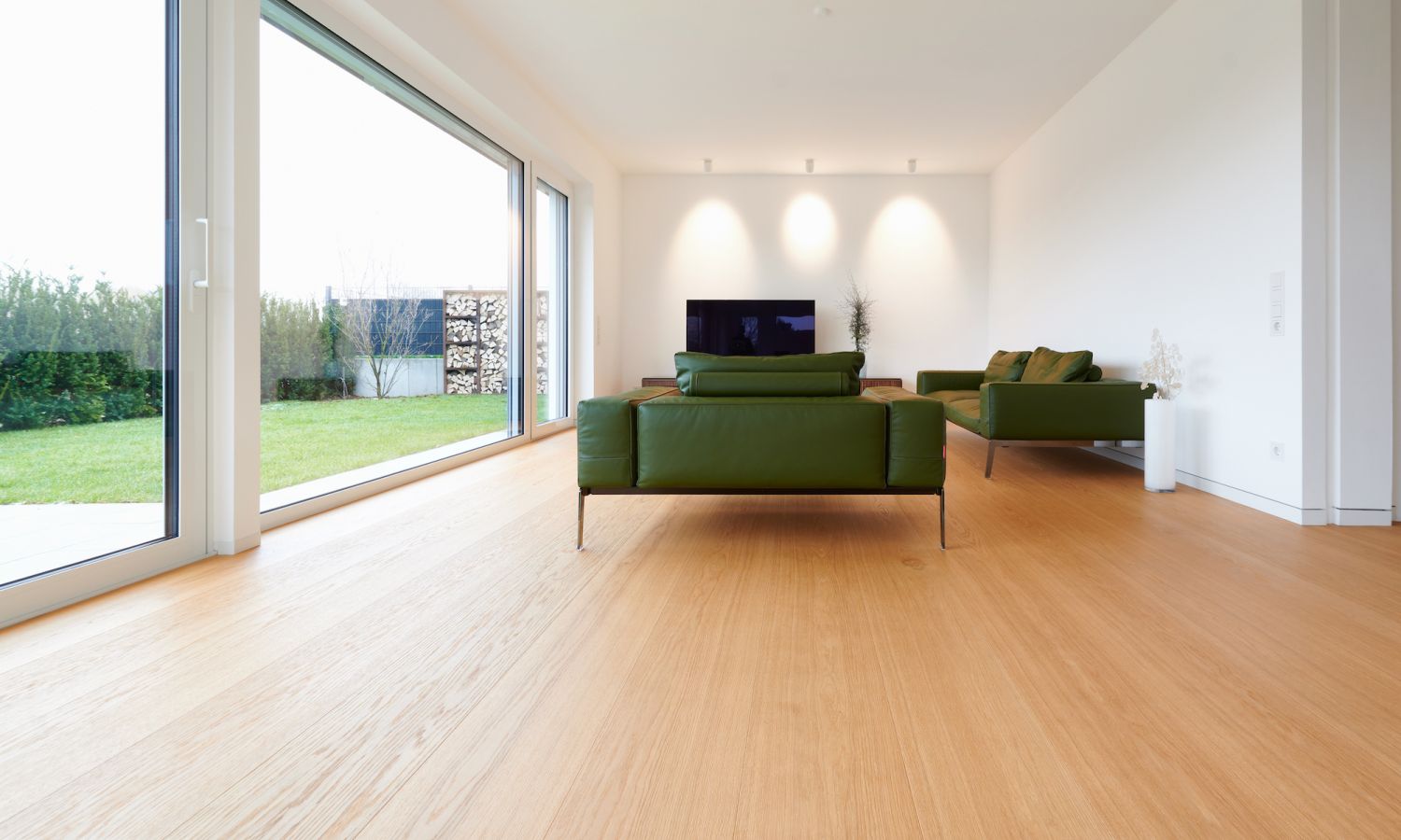 Moderner Wohnraum mit zwei gruenen Sofas, großem Fenster mit Blick auf Garten und Eiche Holzboden.