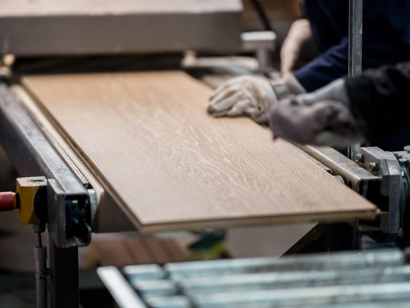 Une lame de chêne sort à moitié d’une machine. On voit la main d’un artisan qui passe un chiffon sur la surface.