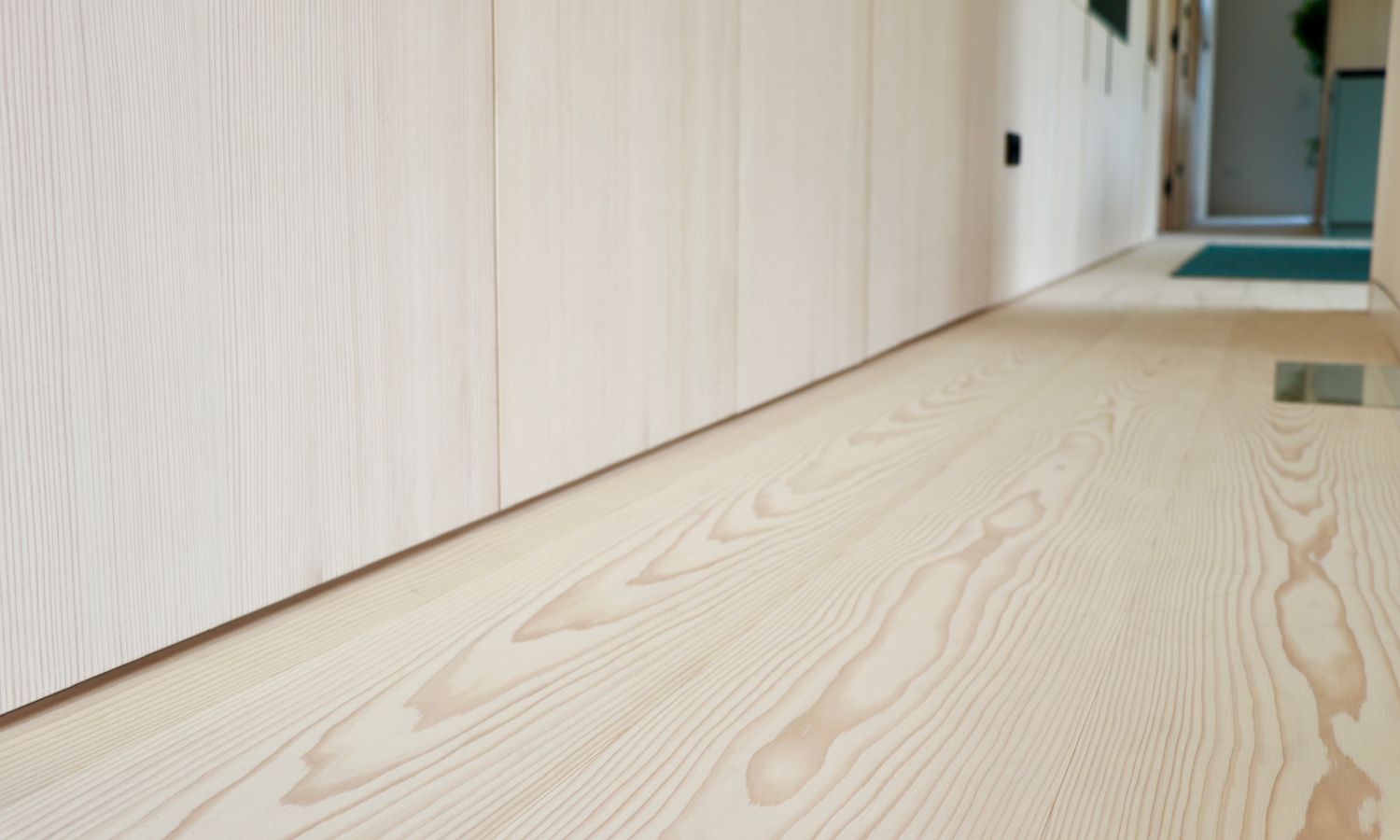 Blick auf einen Weisstanne Holzboden mit sichtbarer Maserung und eine Wand mit hellen Schranktueren in einem Flur.