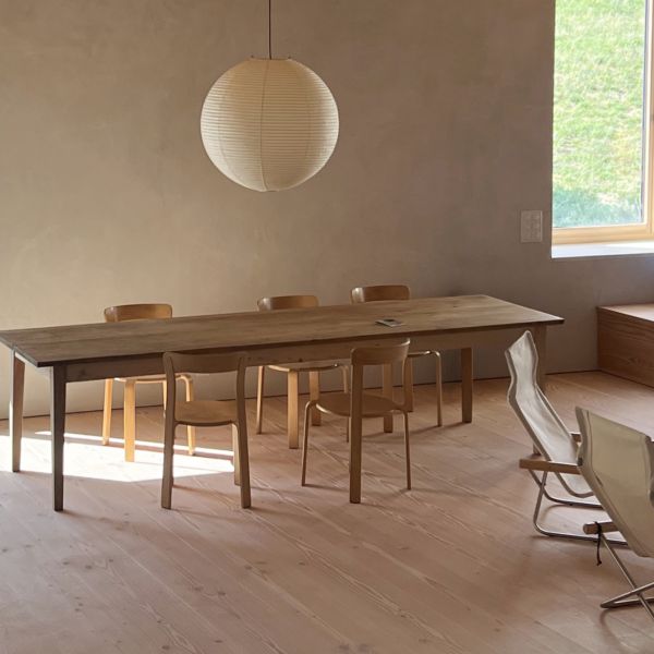 Ein Esszimmer in einem renovierten Bauernhaus mit breiten Dielen aus Douglasie. Darauf steht ein schlichter Holztisch mit modernen Holzstühlen und einer großen weißen, runden Lampe.