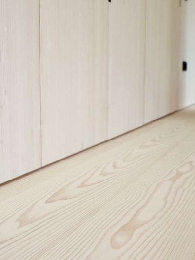 Vue sur un parquet en sapin blanc avec veinures visibles et un mur avec des portes d’armoires claires dans un couloir.