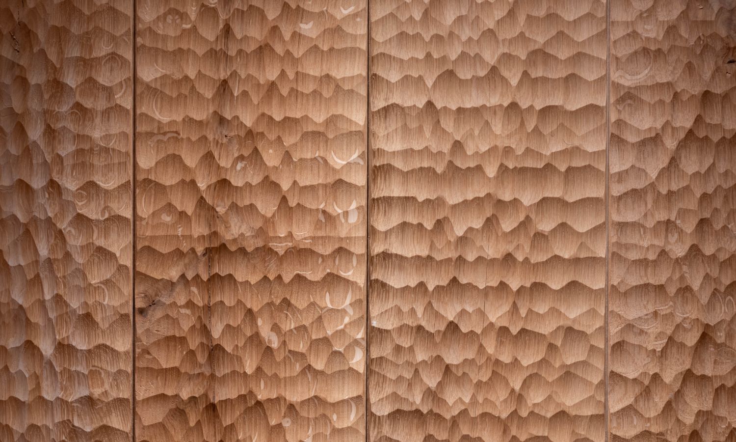 Vue rapprochée des panneaux muraux en chêne. La surface présente une texture ondulée et irrégulièrement rabotée, qui met en valeur le caractère naturel du bois et crée une apparence tactile unique.