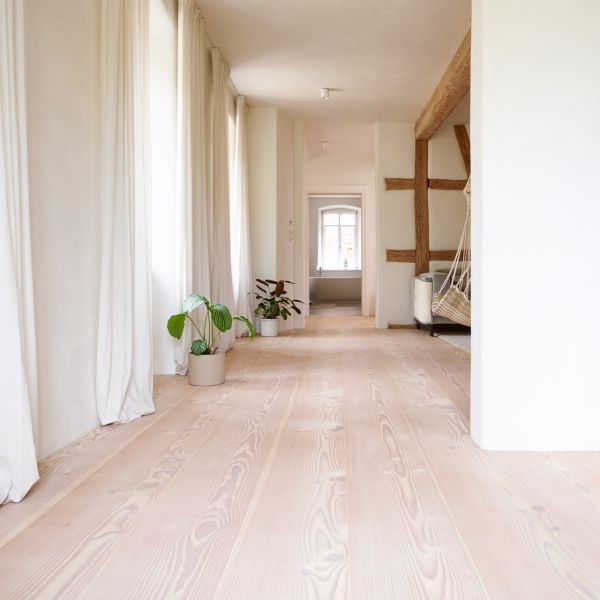Heller Flur mit Douglasie Holzboden; weißen Wänden; weißen Vorhängen; sichtbaren Holzbalken an der Decke und Wand