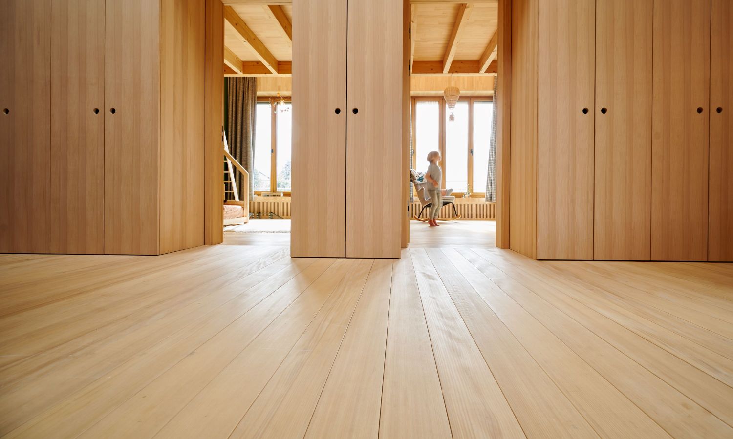 View through a corridor with white fir wooden floors and walls, with a person sitting on a chair in the background.