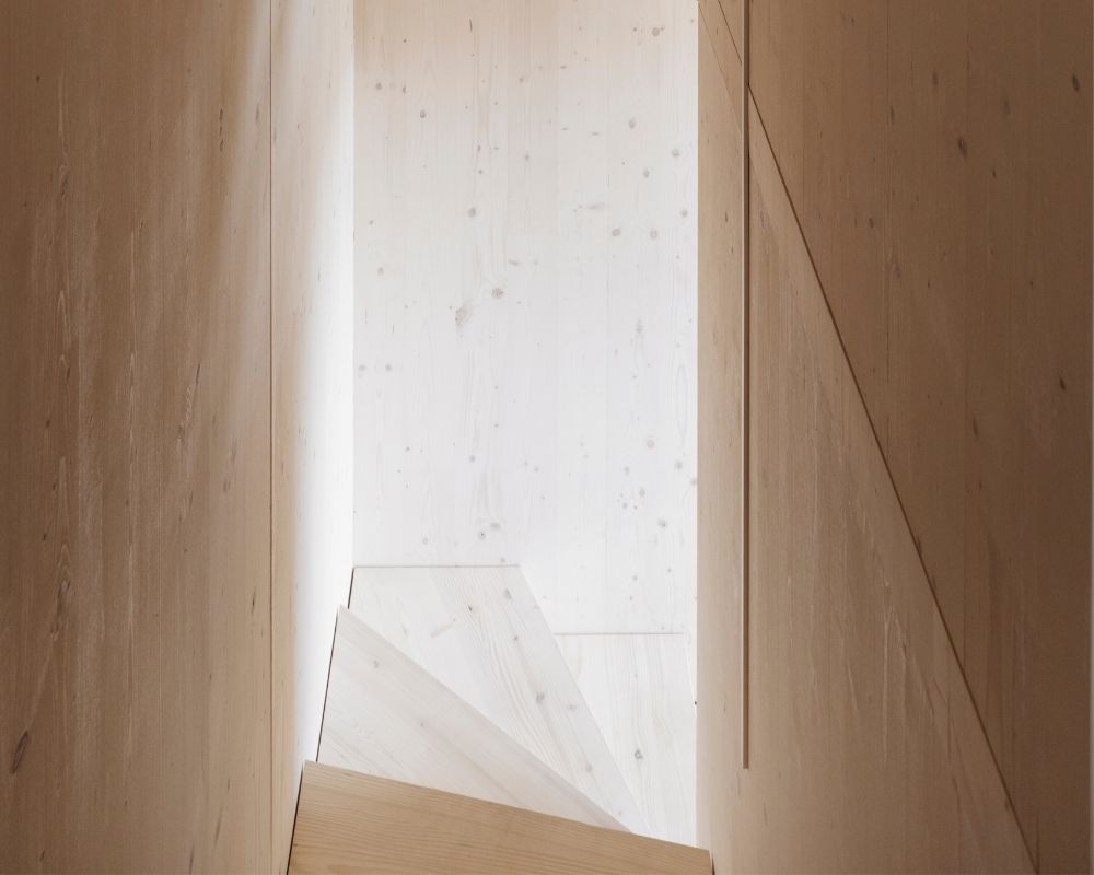 Escalier en bois de sapin blanc avec cage d’escalier etroite et rectangulaire et panneaux de bois clair sur les murs et les marches.