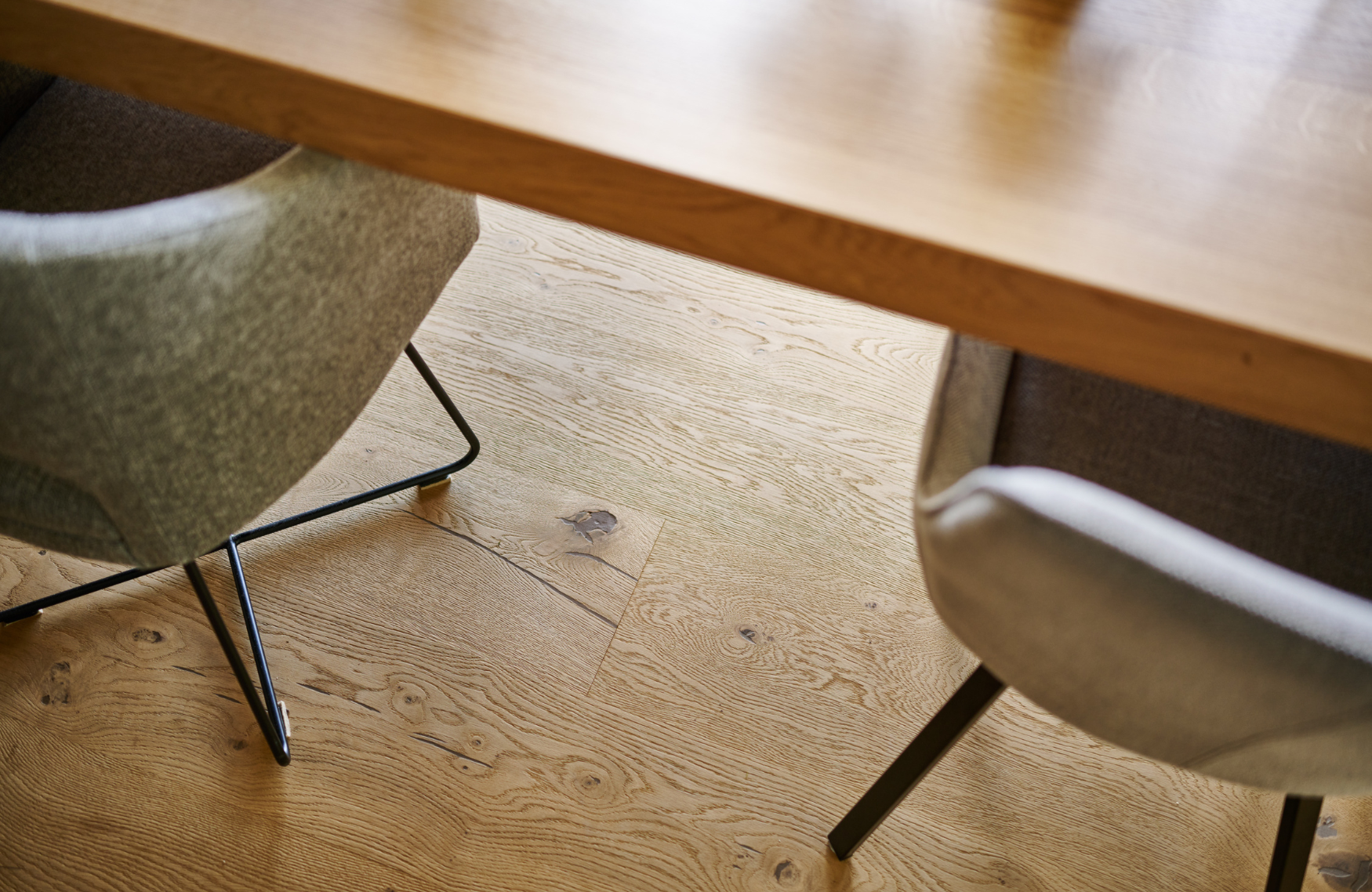 Zwei graue Stuehle mit Metallbeinen stehen an einem Holztisch auf Eiche Holzboden mit sichtbarer Maserung.