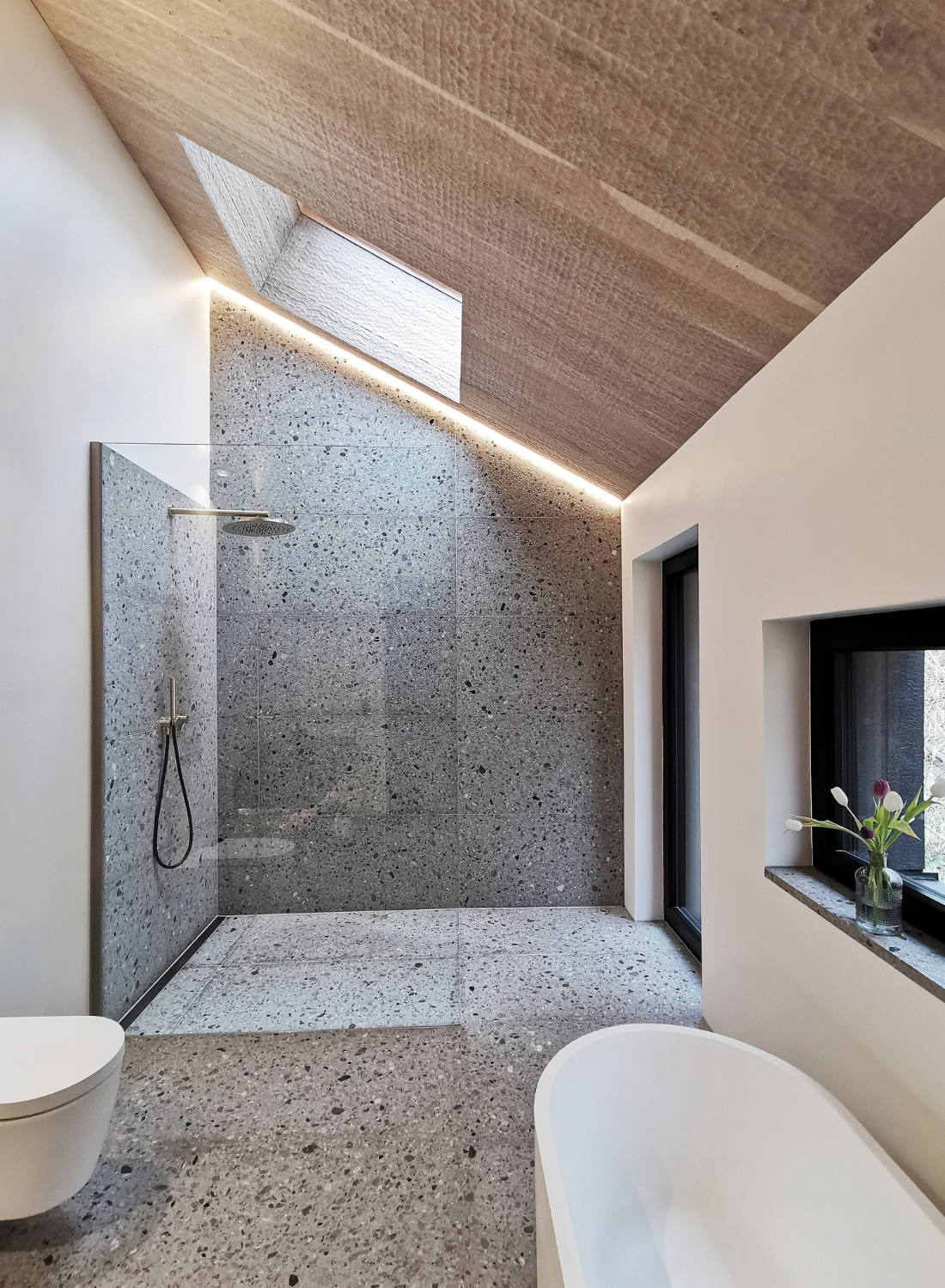 salle de bain moderne avec baignoire indépendante, douche à l’italienne avec cloison en verre et fenêtre de toit sous panneaux muraux en chene inclinés